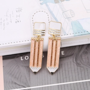 Minimalist pencil shaped earrings with pink enamel and crystals on a white notebook