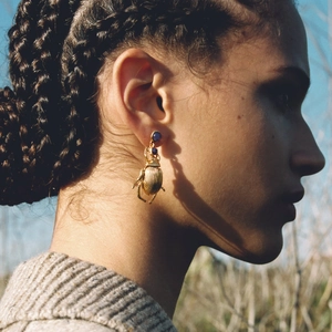 Bohemian gold beetle earrings with blue gemstone worn by model in a side view