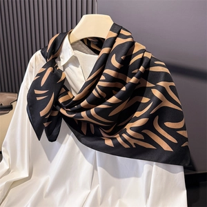 Détail d'un foulard en satin imprimé animal noir et doré porté sur un col de chemise blanc