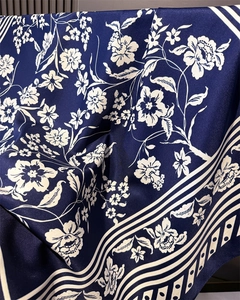Close-up of silk-textured navy blue square scarf featuring white floral and geometric patterns