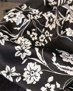 Close-up of premium satin silk fabric with elegant white floral print on a black background