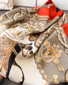 Close-up of equestrian silk scarf featuring horse bits, stirrups, and red border detail
