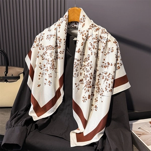 Elegant floral silk scarf in cream and brown stripes draped on a hanger with a handbag