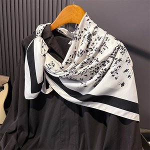 Detailed view of cream silk scarf with black floral print draped on a dark shirt