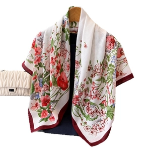 Elegant silk scarf with floral prints and red borders hanging on a wooden hanger