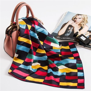 Close-up of geometric silk square scarf with vibrant color blocks draped on a pink handbag