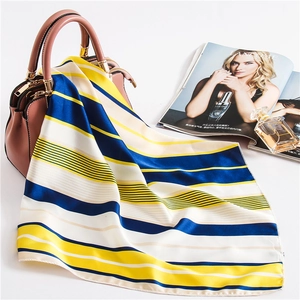 Detail of a striped satin scarf in navy and yellow draped over a pink handbag elegantly
