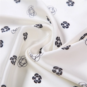 Detailed close-up of white silk scarf featuring elegant black camellia flower patterns