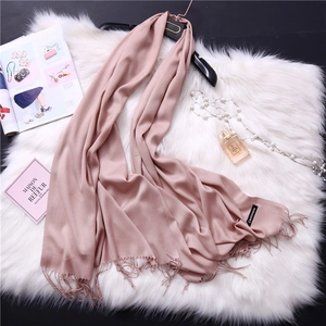 Detail of pink cashmere scarf with fringe hem next to pearls and fashion accessories