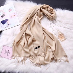 Detail of beige cashmere scarf with elegant tassels on a soft white plush background