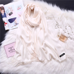 Close-up of cream cashmere scarf with tassels on white plush background with accessories