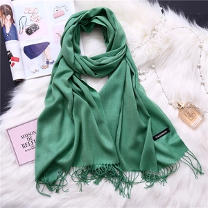 Detail of green cashmere scarf with fringe edges and label on white plush background