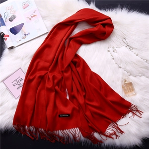 Close-up of red cashmere scarf with fringe and brand label on white fur background