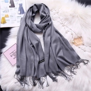 Detailed macro view of soft gray cashmere feel scarf with fringe trim and texture labels