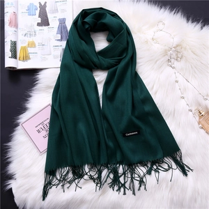 Detailed view of dark green cashmere scarf with fringe and a classic fabric label