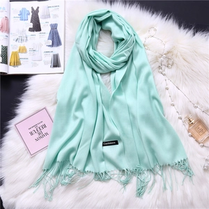 Close-up of mint green cashmere-feel scarf with elegant fringe detail on soft white fur