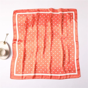 Detailed close-up of a pink satin silk square scarf with white polka dots and elegant trim