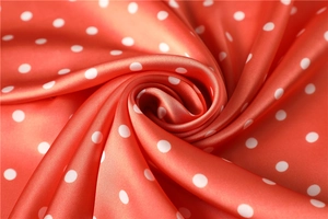 Detailed macro shot of silky satin fabric featuring vibrant orange and white polka dots