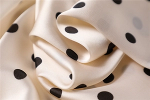 Detailed view of satin silk scarf featuring classic black polka dots on cream fabric