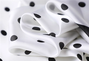Macro view showing smooth satin fabric texture with elegant black polka dots pattern