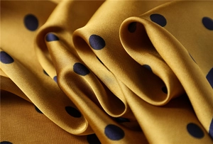 Macro shot of ginger yellow satin silk scarf with black polka dots and smooth texture