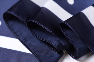 Macro detail of navy blue polka dot silk scarf showing satin texture and rolled hem edges