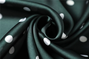 Macro view of dark green polka dot silk satin fabric with elegant drape and glossy texture