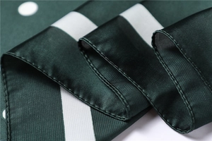 Close-up of dark green satin scarf with white polka dots and detailed hem stitching