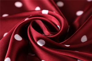 Detailed macro shot of burgundy satin fabric with classic white polka dots and silk-like sheen