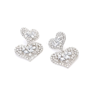 Détail de boucles d'oreilles double cœur argentées avec strass brillants et cristaux