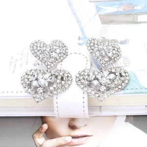 Vue détaillée des boucles d'oreilles cœur en argent avec strass brillants sur cuir blanc