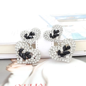 Détail des boucles d'oreilles cœur argentées à étages avec cristaux blancs et gemmes noires
