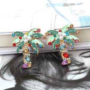 Colorful tropical palm tree earrings with crystal rhinestones and pearls on a notebook
