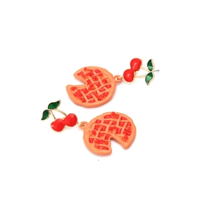 Détail de boucles d'oreilles en émail cerise rouge et tarte orange sur fond blanc