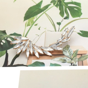 Golden wing ear cuff with marquise rhinestones on a decorative wooden display