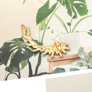 Detail view of gold wing ear cuff with pin and clip closure on a botanical background