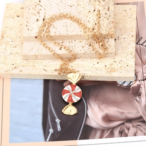 Golden candy pendant necklace with red crystals on beige travertine stone display