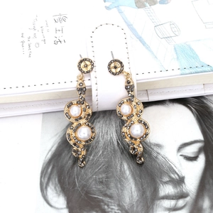 Vintage gold snake earrings with black rhinestones and pearls on a white notebook