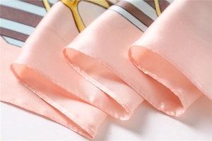 Close-up of pink silk square scarf showing detailed stitching and smooth fabric texture