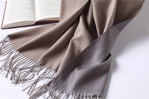Detail of two-tone beige and grey cashmere scarf with elegant fringe trim on a table