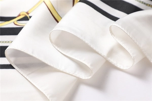 Close-up of white satin scarf with black stripes, golden chain patterns and soft folds