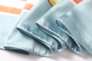 Detailed close-up of machine-rolled hem and geometric orange stripes on silk scarf