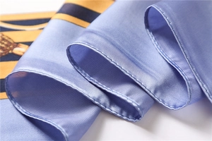 Close-up of sky blue silk scarf with golden stripe border and hand-rolled hem detail