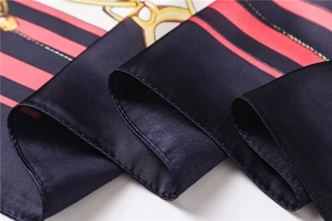 Close-up of silk scarf with red and black stripes, golden chain print and satin finish