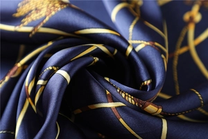 Close-up of silk scarf with golden chain pattern on dark blue satin fabric texture
