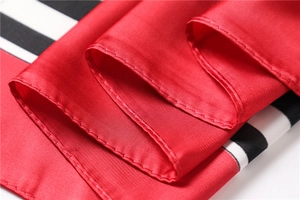 Close-up of silk-textured satin scarf showing fine hem stitching and red-black stripes