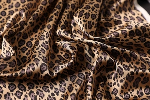 Macro detail of glossy leopard print silk-like satin fabric with smooth folds