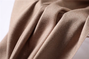 Macro detail of camel cashmere scarf showing soft twill weave texture and warm draped fabric