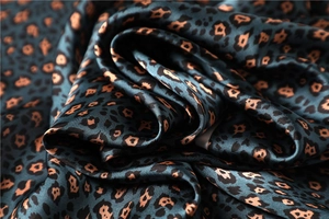 Macro shot of dark green leopard print satin fabric showing silky texture and glossy sheen