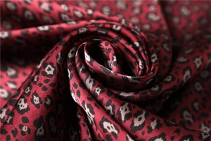 Detail of silk-like dark red leopard print fabric with smooth satin sheen and soft texture